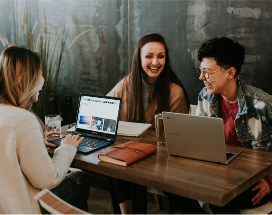Collaborating for Success: Building Income Streams Together Three people laughing and collaborating with laptops at a wooden table, symbolizing teamwork and creating income streams online.
