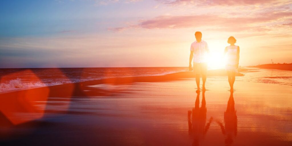 Romantic Sunset Stroll on the Beach A couple walking hand in hand on a beach during sunset, with the sun casting a warm glow on the sand and waves.